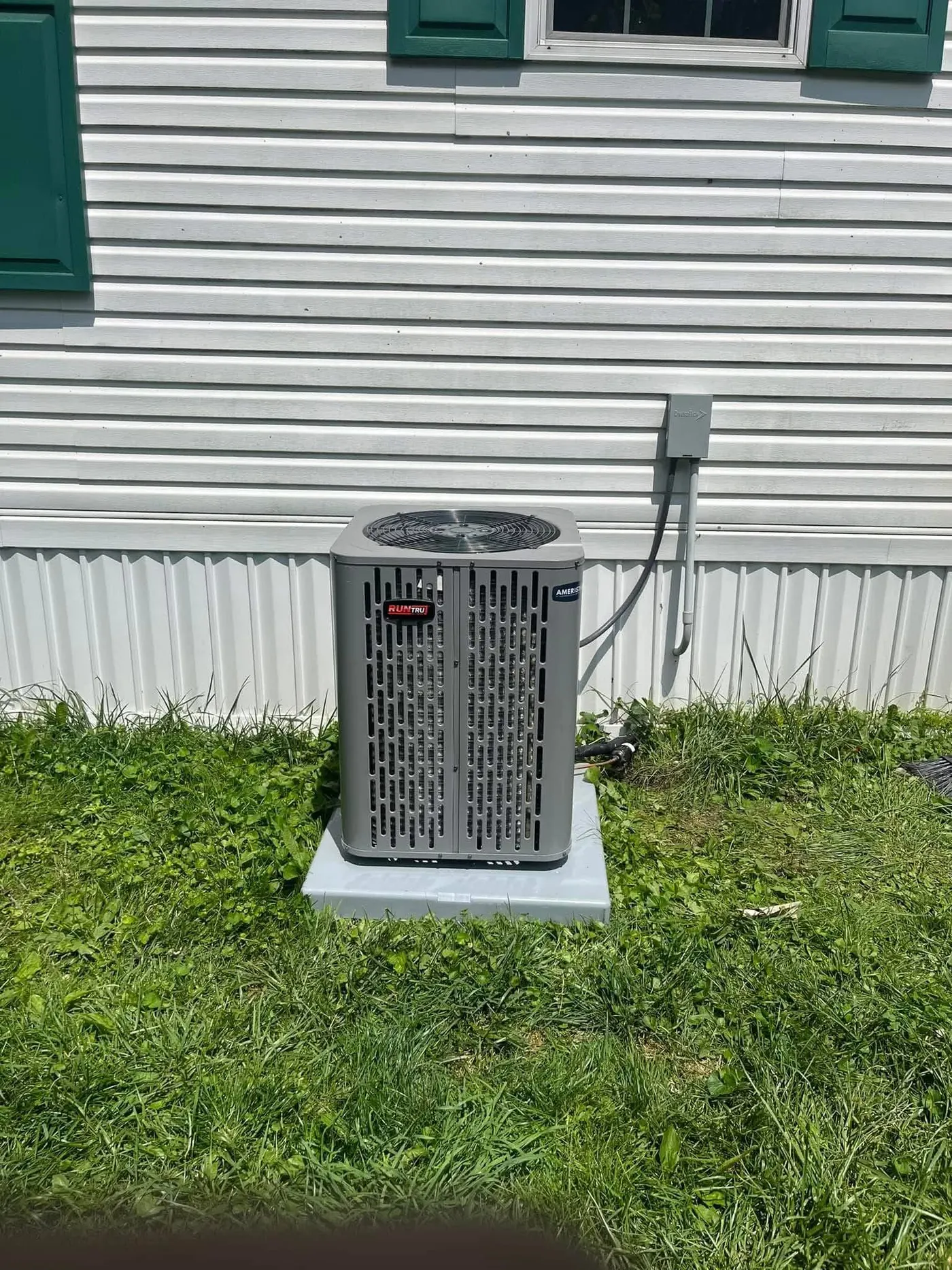 A new RunTru by Trane air conditioning condenser on a composite pad beside white vinyl siding